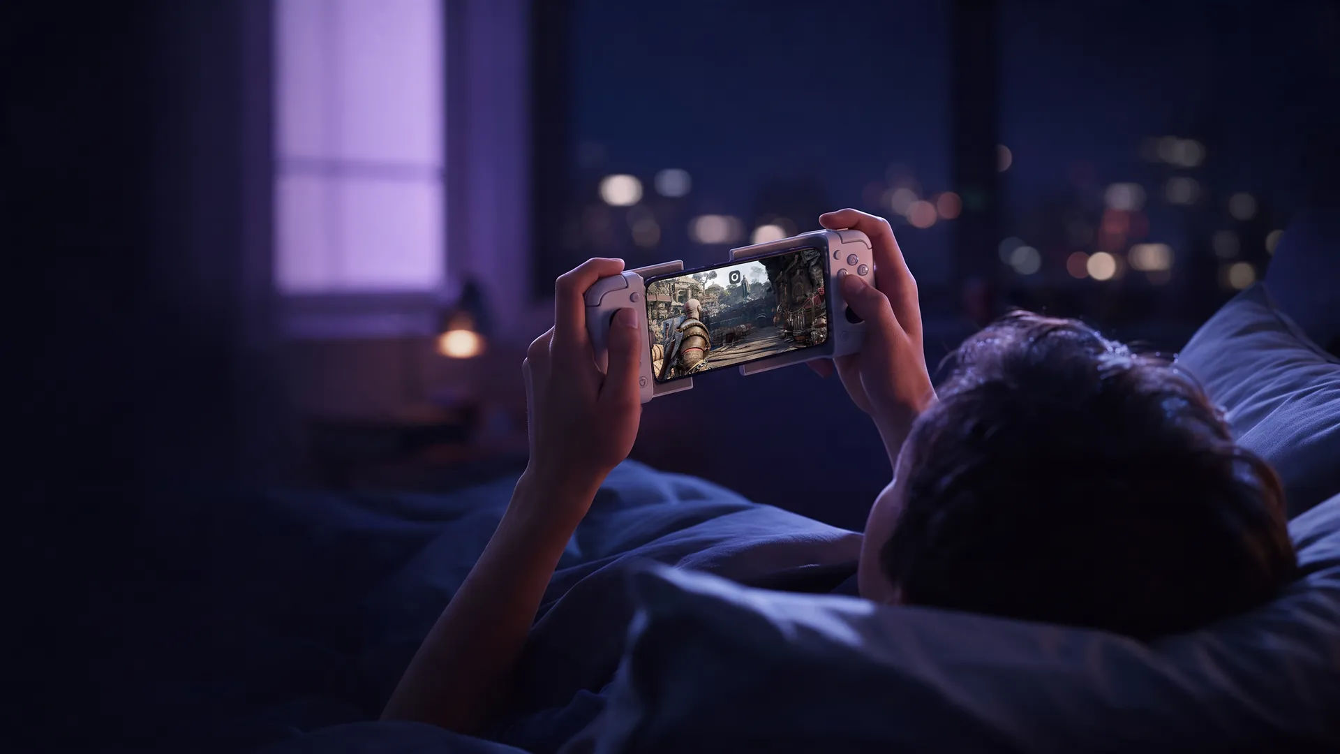 A player in bed at night playing God of War on an iPhone in a controller