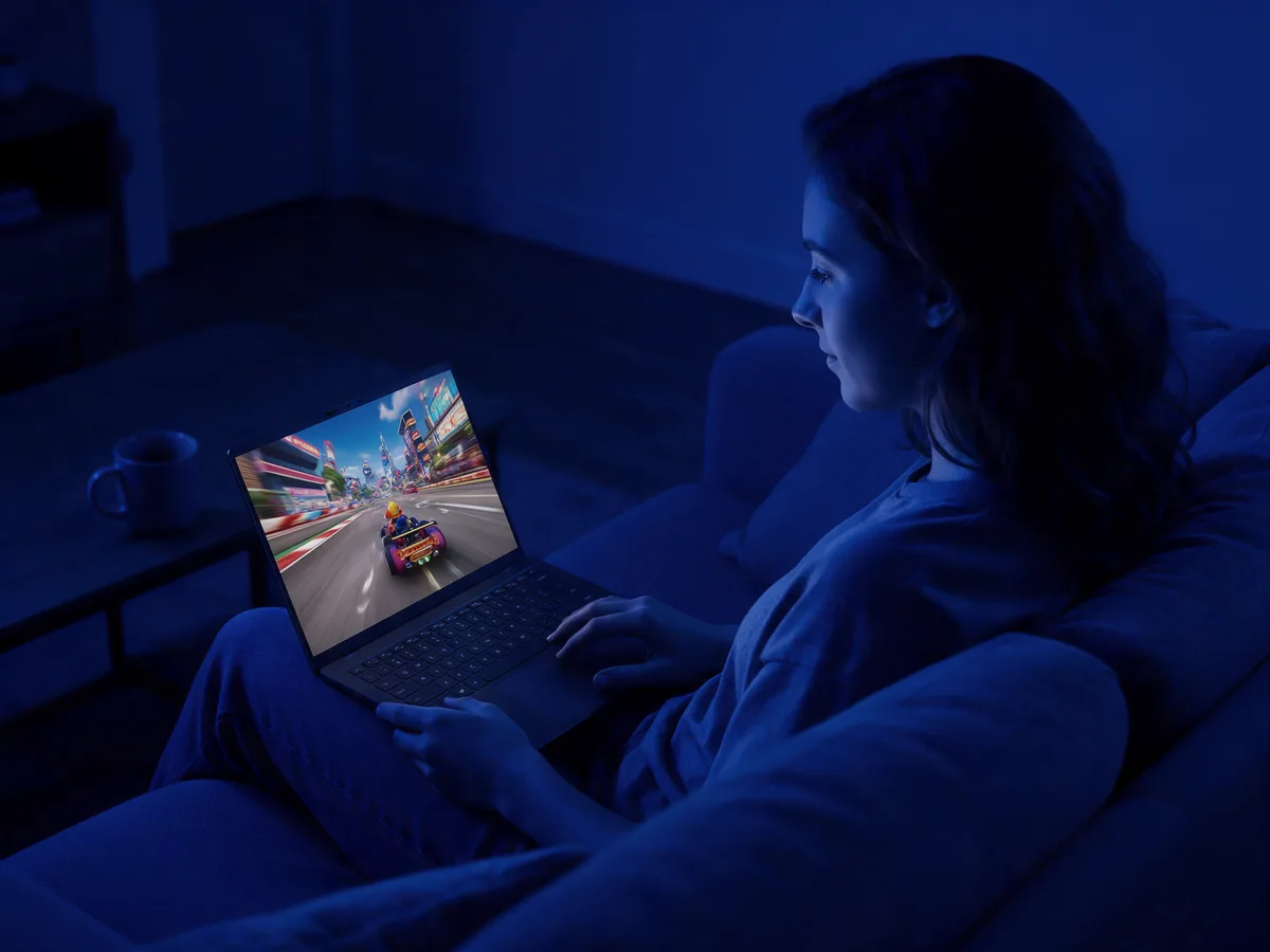 A woman on the sofa playing a racing game on her laptop