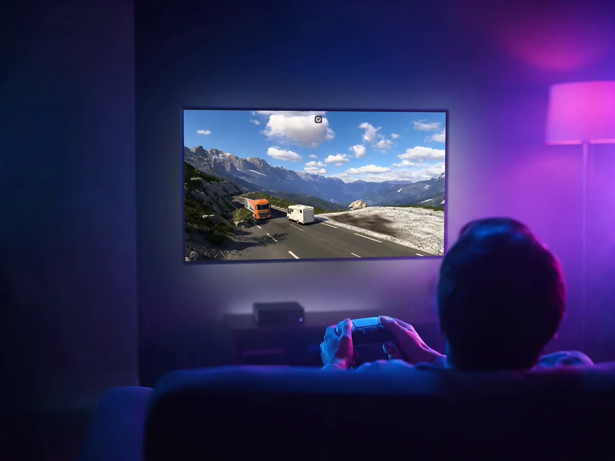 A player on the sofa with a controller, a truck driving game on the TV and a streaming box below it